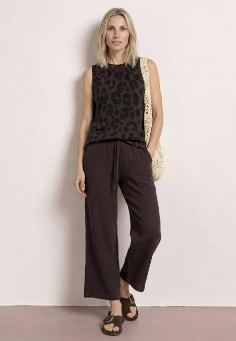 Top mit Rundhals und Zebra-Print molten earth Frau trägt ärmelloses Leoparden-Top, weite schwarze Hose, Sandalen und Basttasche.