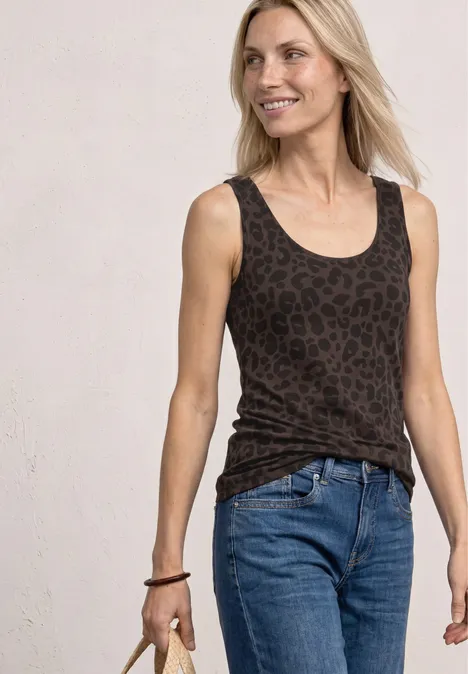 Vrouw in spijkerbroek en donker luipaardprint top voor een lichte achtergrond.