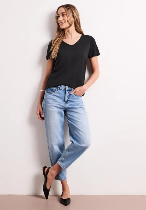 Een vrouw poseert nonchalant in een zwart T-shirt en lichtblauwe jeans voor een neutrale achtergrond.