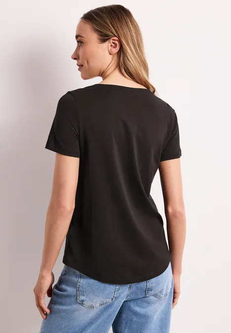 Frau von hinten in schwarzem T-Shirt und blauen Jeans vor hellem Hintergrund.