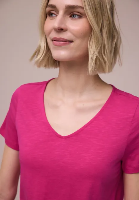 Eine Person trägt ein pinkfarbenes T-Shirt vor hellem, neutralem Hintergrund.