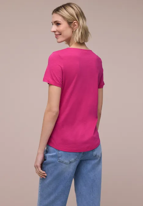 Frau von hinten in pinkem T-Shirt und blauen Jeans vor neutralem Hintergrund.