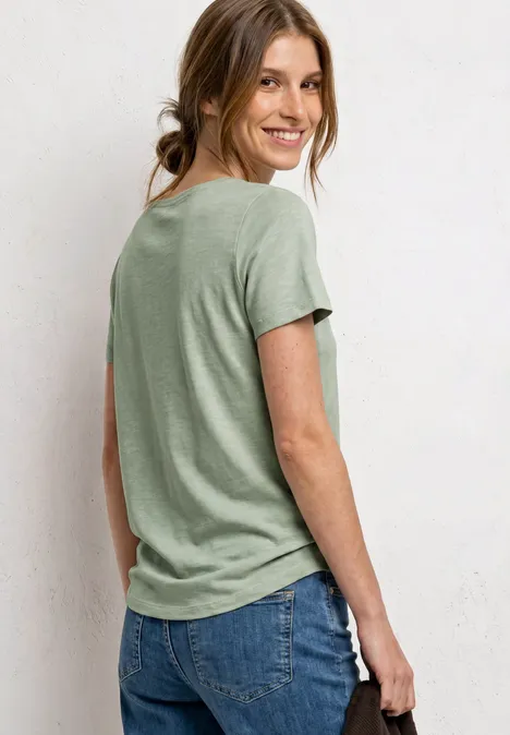 Eine Person steht mit dem Rücken zur Kamera, trägt hellgrünes T-Shirt und Jeans.