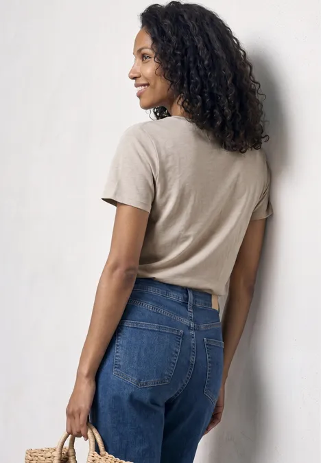 Basic T-Shirt mit V-Neck in Unifarbe light sepia sand Frau von hinten in beigefarbenem T-Shirt, blauen Jeans und Strohtasche in der Hand.