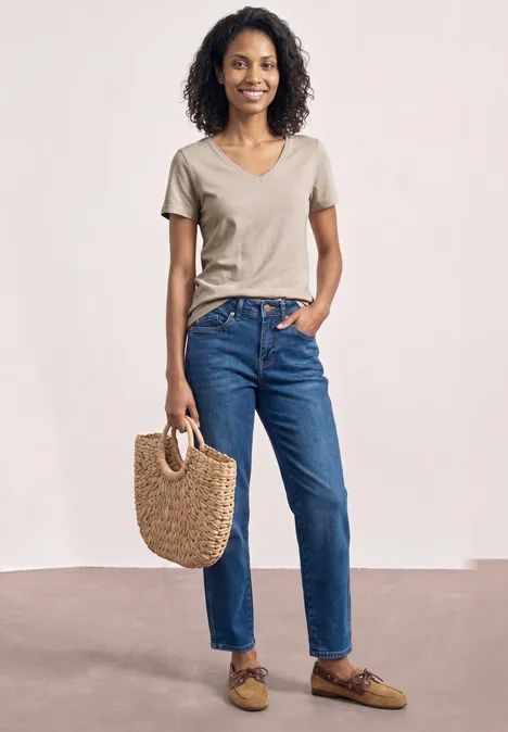 Basic T-Shirt mit V-Neck in Unifarbe light sepia sand Frau mit lockigem Haar in beigem T-Shirt, blauen Jeans und braunen Loafers hält eine Strohtasche