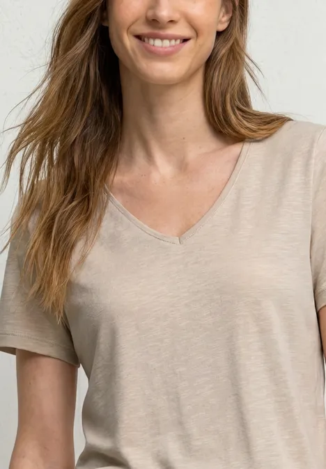 Basic T-Shirt mit V-Neck in Unifarbe light sepia sand Eine lächelnde Frau in einem beigen, kurzärmeligen V-Ausschnitt-Oberteil, halbe Körperansicht.