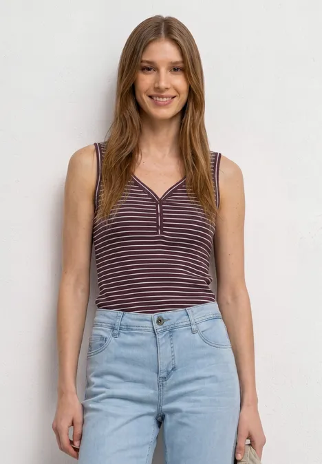 Top mit V-Neck und Streifen rustic rouge Frau steht vor hellem Hintergrund und trägt ein gestreiftes Top und eine helle Jeans.
