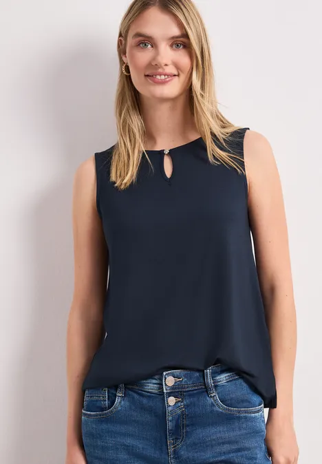 Frau trägt ärmelloses dunkelblaues Top und blaue Jeans.