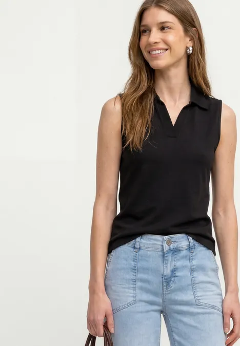Frau mit schwarzem ärmellosen Oberteil und hellblauen Jeans vor hellem Hintergrund.