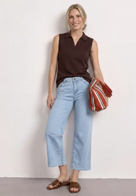 Vrouw in donkerbruin mouwloos topje, lichtblauwe wijde jeans, bruine sandalen en gestreepte tas.