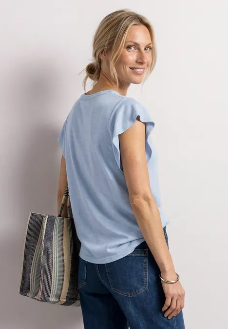 Shirt met korte volantmouwen cashmere blue Vrouw in lichtblauw topje en spijkerbroek, met gestreepte tas over haar schouder.