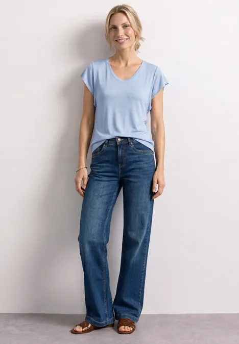 Shirt met korte volantmouwen cashmere blue Vrouw in lichtblauw t-shirt en wijdvallende jeans voor lichte achtergrond