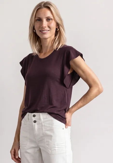 Shirt mit kurzen Volant-Ärmeln rustic rouge Eine Frau in einem violetten T-Shirt mit Rüschenärmeln und hoch geschnittenen cremefarbenen Hosen in lässiger Pose
