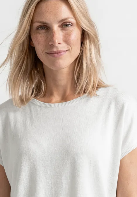 Une femme aux cheveux blonds mi-longs porte un t-shirt blanc.