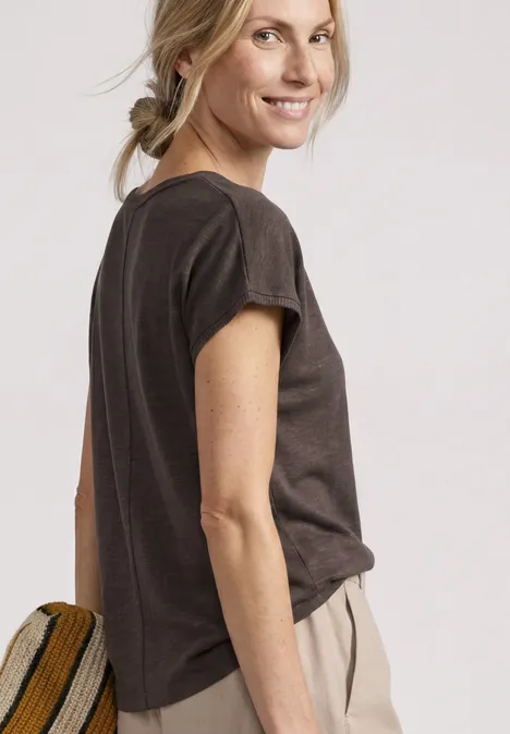 Chemise dropped shoulder à col rond espresso brown Profil d'une femme en t-shirt foncé et pantalon clair, cheveux en tresse, fond uni.