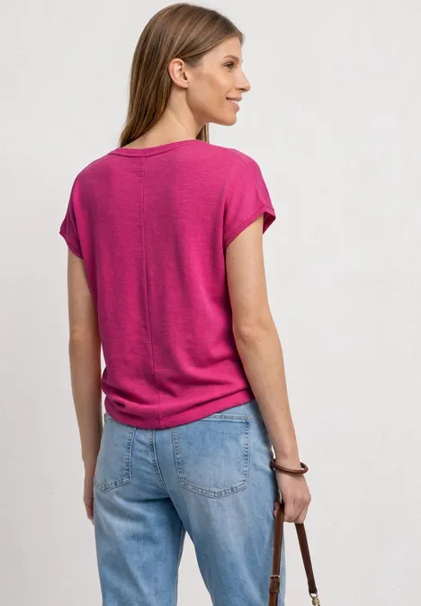 Eine Frau in pinkem T-Shirt und blauer Jeans mit Tasche, von hinten zu sehen.
