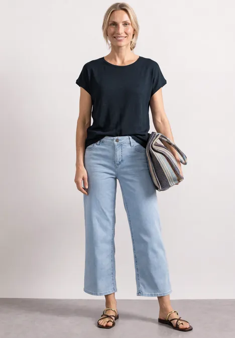 Dropped Shoulder Shirt mit Rundhals shadowed navy Frau trägt schwarzes T-Shirt, hellblaue, weite, knöchellange Jeans, Sandalen und gestreifte Tasche.