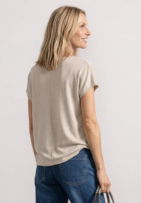Frau von hinten in beigem T-Shirt und Jeans, hält eine Handtasche in der rechten Hand.