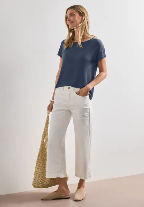Dropped Shoulder Shirt mit Rundhals ashen blue Frau in lässigem Outfit mit dunkelblauem T-Shirt, weißer Culotte, beigen Slippern und geflochtener Tasche.