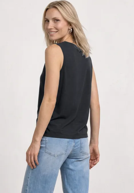 Een vrouw van achteren in een zwarte mouwloze top en blauwe spijkerbroek.