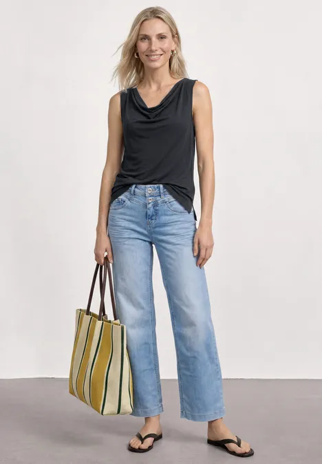 Vrouw met zwarte mouwloze top, lichtblauwe wijde jeans, zwarte slippers en gestreepte shopper in groen en beige.