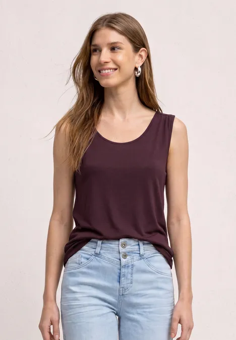 Top aus Jersey mit Elastiksaum rustic rouge Frau mit ärmellosem dunkelrotem Top und hellblauen Jeans vor hellem Hintergrund