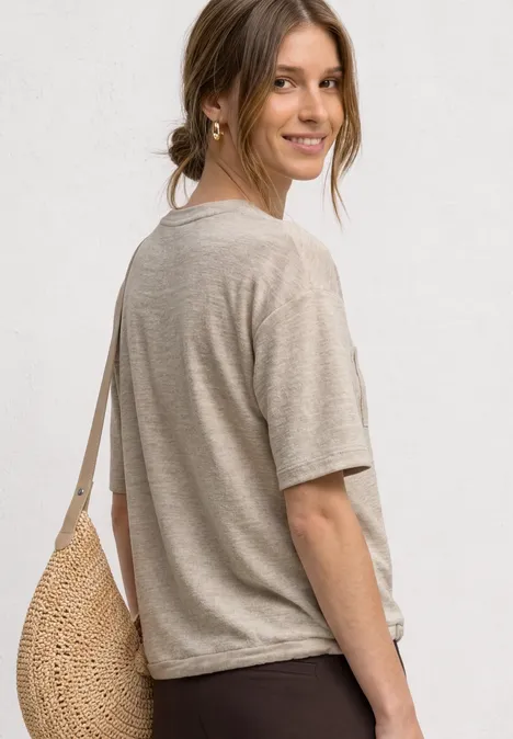 T-Shirt mit Rundhals und Brusttasche clay sand Junge Frau von der Seite mit beigem T-Shirt, Strohtasche über der Schulter vor weißem Hintergrund.
