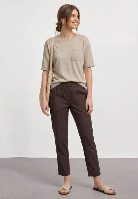 T-Shirt mit Rundhals und Brusttasche clay sand Frau in beigem T-Shirt, braunen Hosen und Sandalen mit Umhängetasche