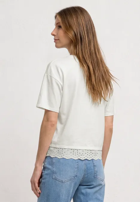 Shirt met ronde hals en kant off white Een vrouw van achteren in een wit T-shirt met korte mouwen, met kanten zoom en blauwe spijkerbroek.
