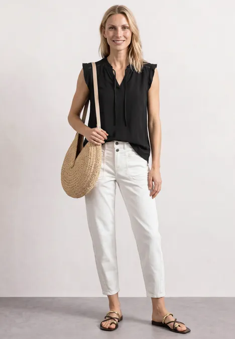 Frau in schwarzem ärmellosen Top, weißen Jeans, schwarzen Sandalen und runder Strohtasche.