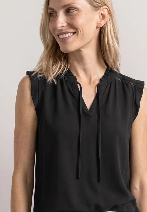 Blonde Frau in schwarzem ärmellosem Oberteil lächelt leicht zur Seite.