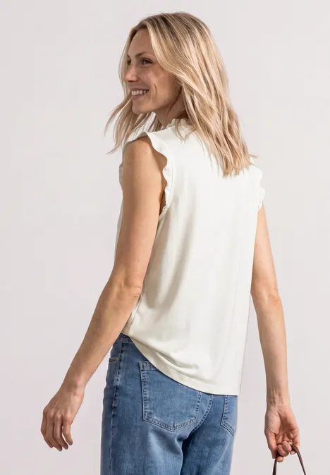 Frau von hinten mit blonden Haaren, trägt ein ärmelloses Top, Jeans und hält eine dunkle Clutch.