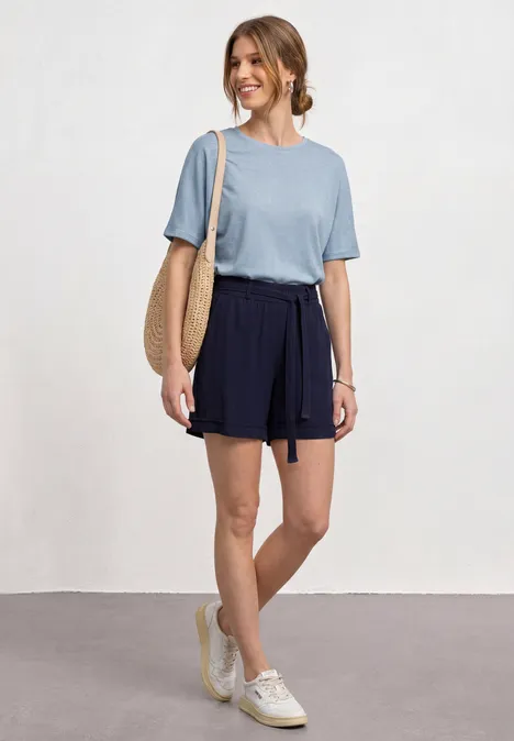 Vrouw met blauw t-shirt, donkerblauwe short, strozak en witte sneakers.