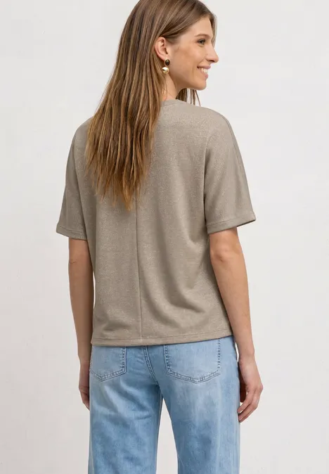 Shirt met overhangende schouders en glitterdetails clay sand Vrouw van achteren in beige T-shirt en blauwe spijkerbroek.