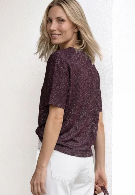 Chemise dropped shoulder avec détails scintillants rustic rouge Une personne de dos porte un T-shirt pailleté et un jean blanc devant un fond blanc.