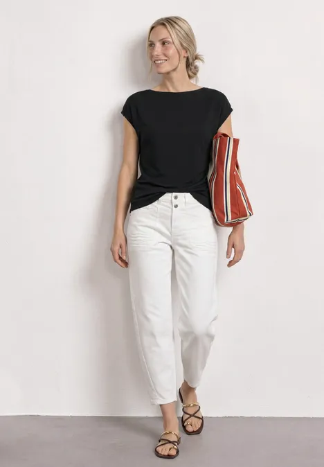 Dropped Shoulder Shirt mit Raffung Black Person in schwarzem Shirt, weißer Hose und Sandalen mit rot-orange gestreifter Tasche vor weißem Hintergrund.