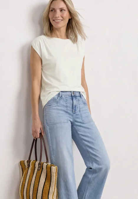 Shirt met overhangende schouders en rimpels off white Vrouw in witte t-shirt, lichtblauwe jeans en gestreepte tas voor een witte achtergrond.