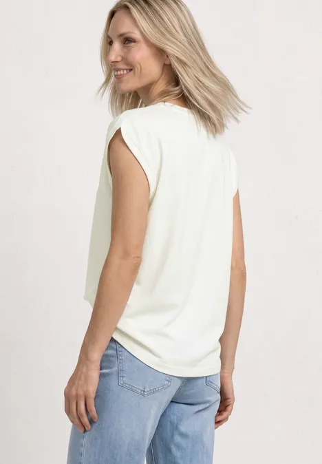 Shirt met overhangende schouders en rimpels off white Vrouw van achteren in een wit mouwloos shirt en lichtblauwe jeans, kijkend over haar schouder.