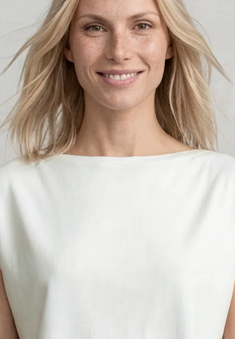 Shirt met overhangende schouders en rimpels off white Vrouw met halflang blond haar in een wit mouwloos topje voor een lichte achtergrond.
