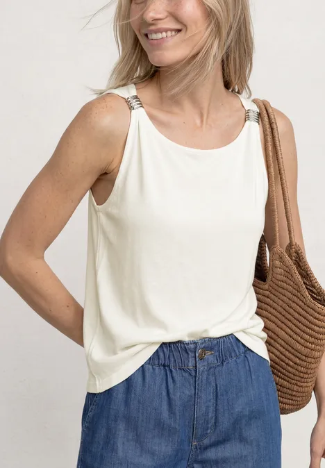Frau in weißem ärmellosem Top und blauen Jeans, mit geflochtener Tasche über der Schulter.