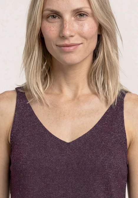 Vrouw met halflang blond haar in een mouwloos paars V-hals top voor een lichte achtergrond.
