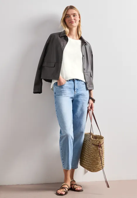 Shirt mit Rundhals und Rippdetails off white Frau mit weißem Top, dunkler Jacke über den Schultern, hellen Jeans, Sandalen und geflochtener Basttasche