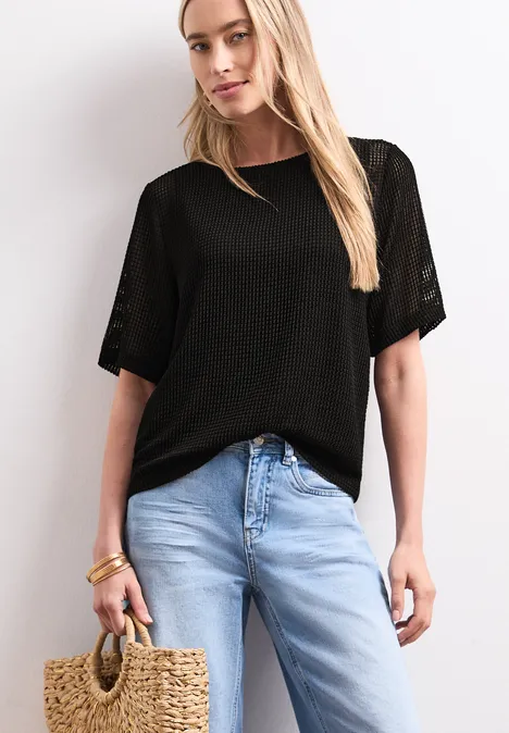 2-in-1 Shirt aus Mesh mit U-Boot-Ausschnitt Black Frau in schwarzem Oberteil, hellen Jeans, mit Strohtasche vor weißem Hintergrund.