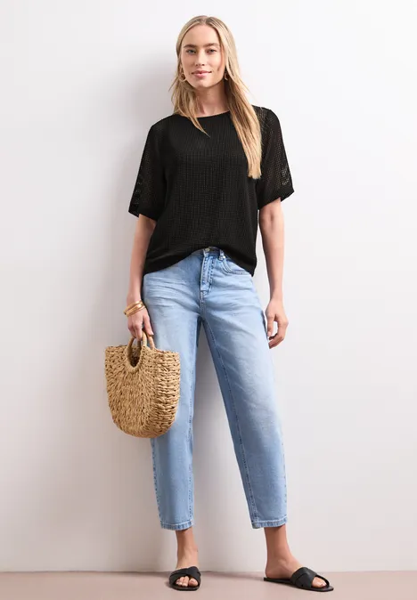 2-in-1 Shirt aus Mesh mit U-Boot-Ausschnitt Black Eine schlanke Frau trägt ein schwarzes T-Shirt, helle Jeans, schwarze Sandalen und hält eine Basttasche.