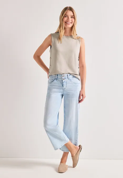 Top mit seitlichen Knopfdetails clay sand Frau in hellem Top, hellblauen Jeans und beigen Espadrilles vor weißem Hintergrund.