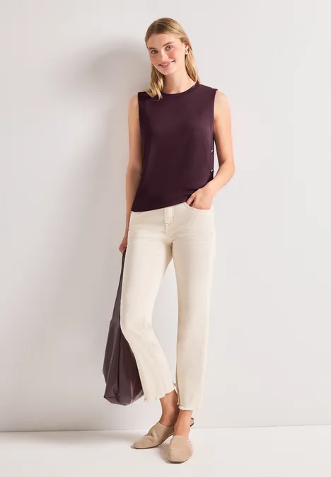 Femme portant un débardeur violet et un pantalon crème, avec un grand sac assorti et des mocassins.