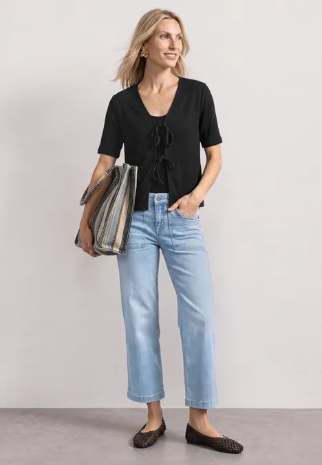 Veste en maille avec rubans Black Femme portant un t-shirt noir à manches courtes, un jean bleu clair, des ballerines marron et un cabas rayé.