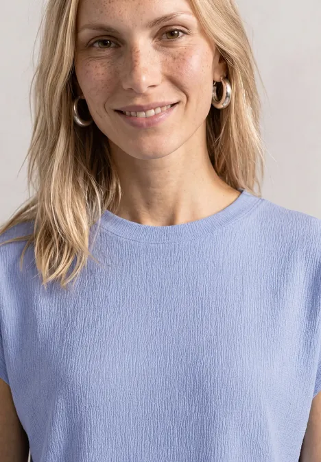 Dropped Shoulder Shirt mit Strukturmix cashmere blue Eine Frau mit blonden Haaren trägt ein hellblaues ärmelloses Oberteil und silberne Creolen.