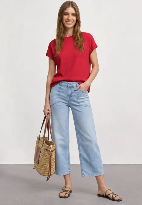 Dropped Shoulder Shirt mit Strukturmix salsa red Frau trägt rotes T-Shirt, hellblaue, weite Cropped-Jeans, schwarze Sandalen und Bast-Shopper vor neutralem Hintergrund.