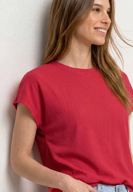 Dropped Shoulder Shirt mit Strukturmix salsa red Frau lehnt an weißer Wand und trägt rotes Kurzarmshirt mit Jeans.
